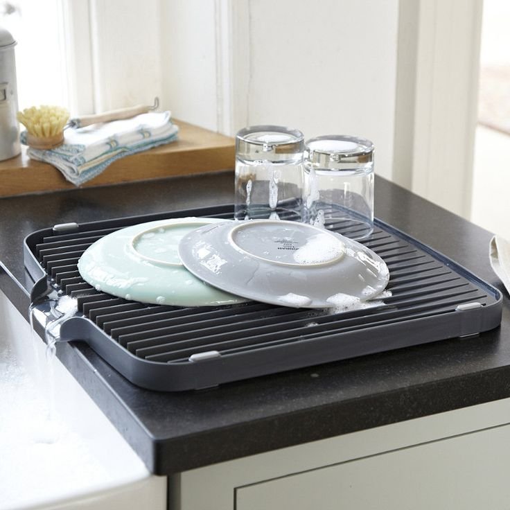 A multi-tier dish rack placed next to the sink, holding various dishes and utensils with a draining board directing water back into the sink.